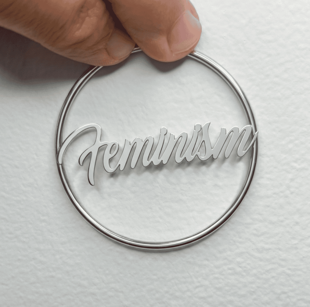 Silberne Feminism Creole 60mm am Ohr getragen – großer Edelstahl-Ohrring mit Schriftzug von Bling Bling Feministas