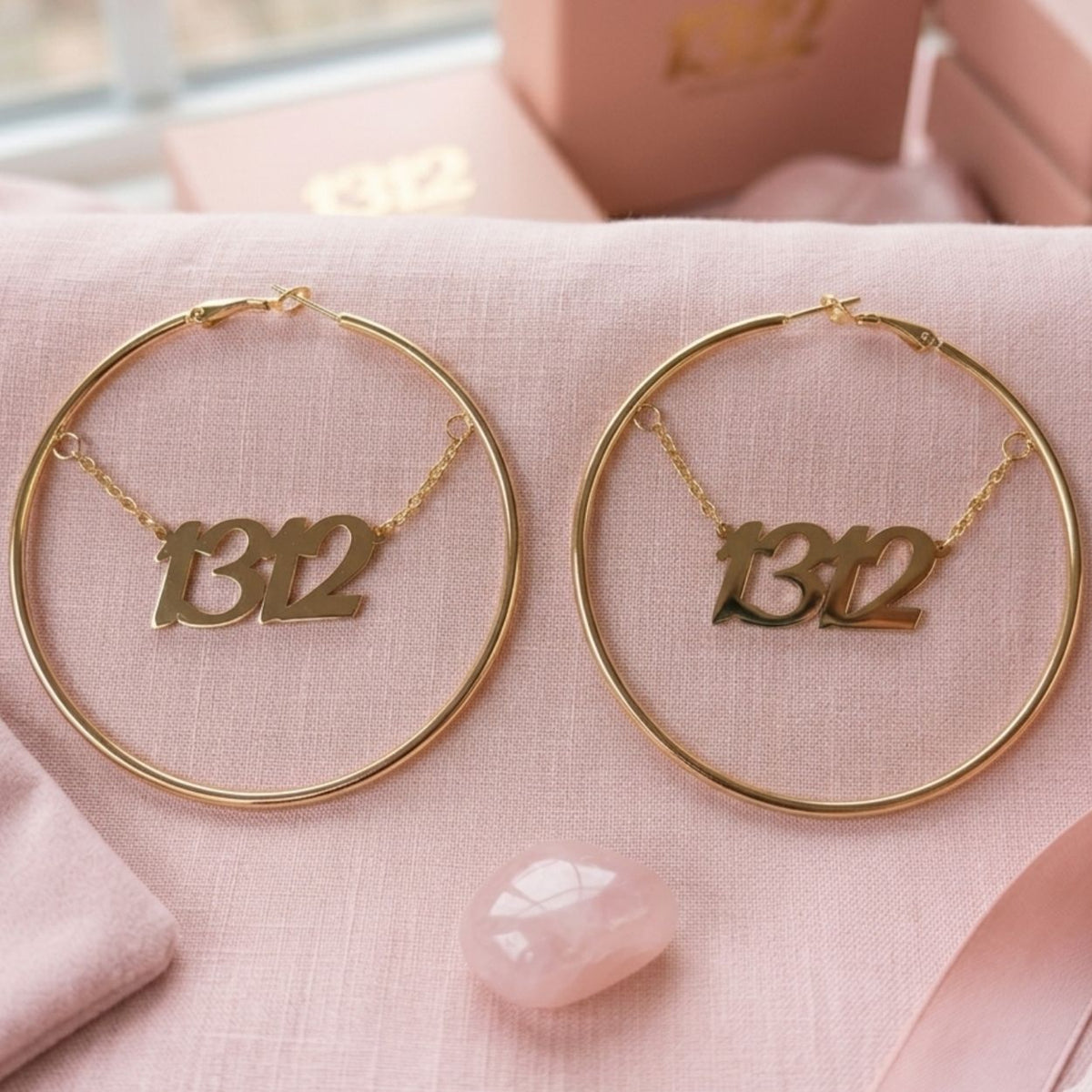 Paar 1312 Creolen in Gold aus Edelstahl, 60 mm, mit 1312-Schriftzug an feiner Kette auf rosa Stoff