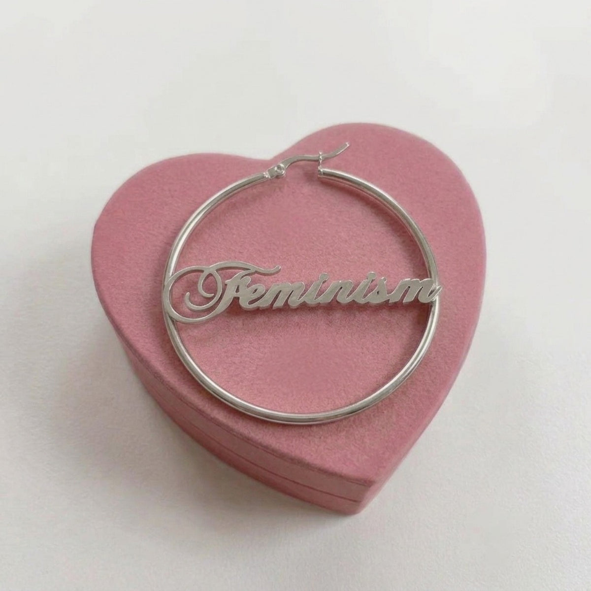 Feminism Creole in Silber aus Edelstahl, 60 mm, mit geschwungenem Schriftzug Feminism auf rosa Herzschachtel
