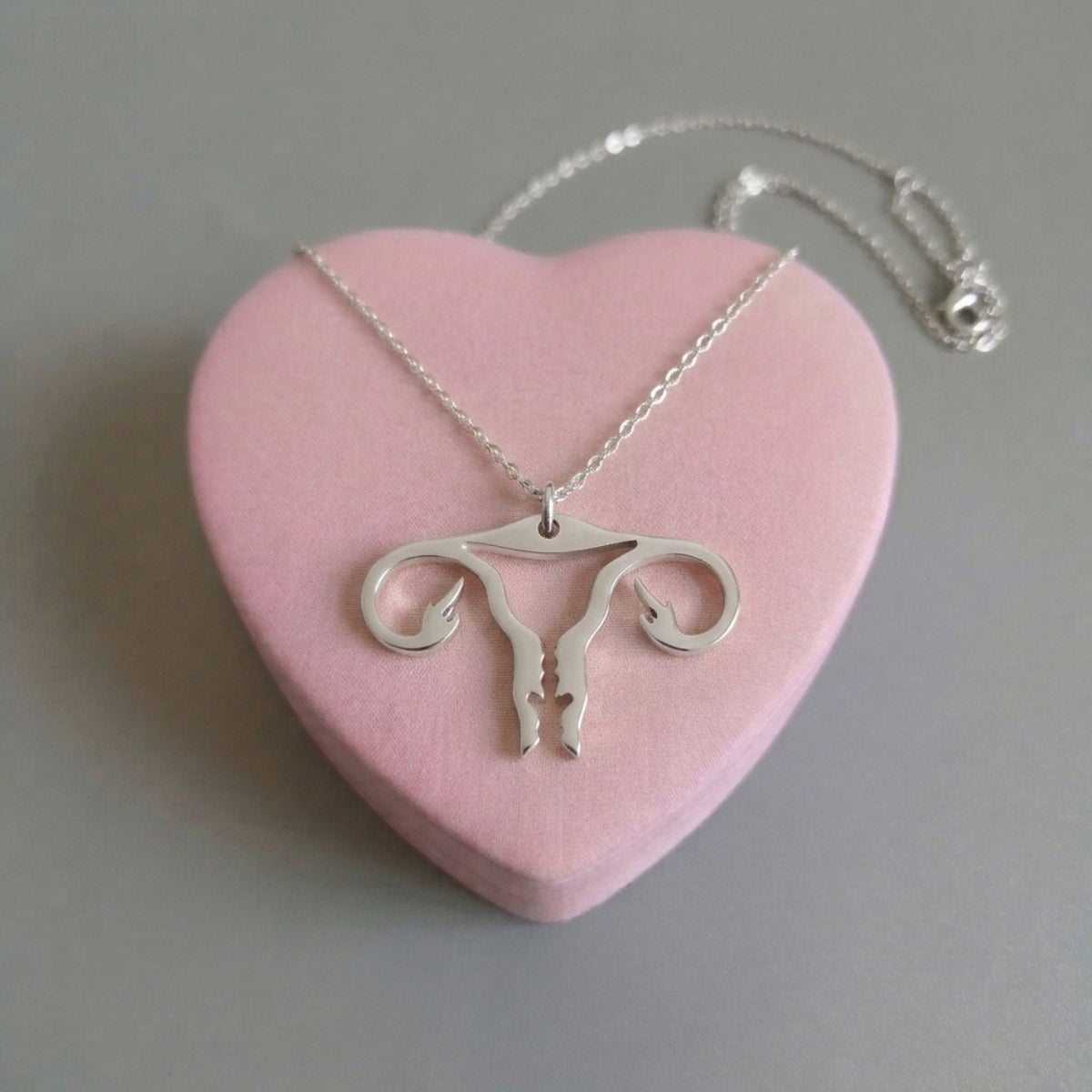 Uterus-Halskette in Silber aus Edelstahl mit Gebärmutter-Anhänger und Mittelfinger auf rosa Herz
