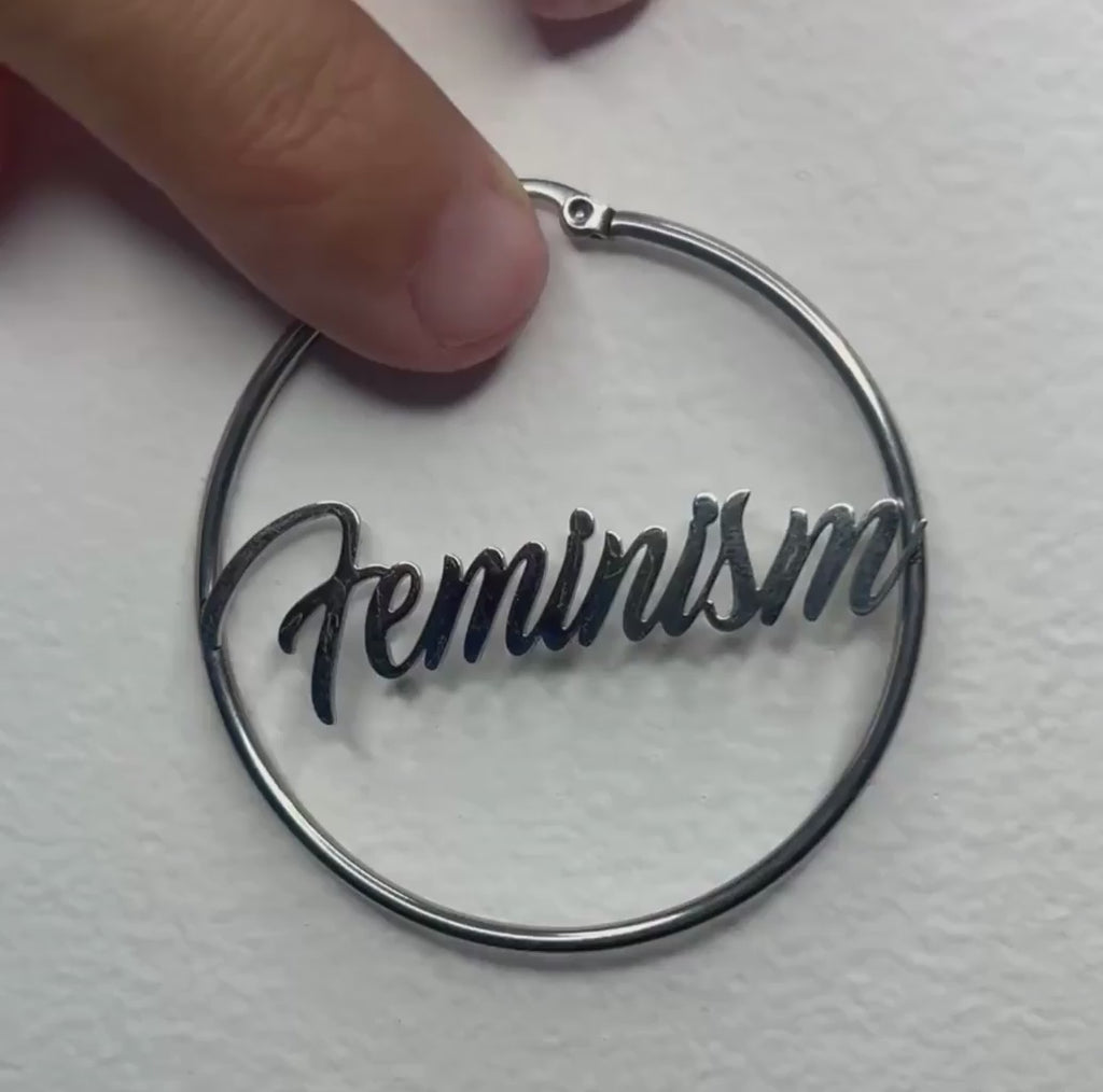 Silberne Feminism Creole 60mm am Ohr getragen – großer Edelstahl-Ohrring mit Schriftzug von Bling Bling Feministas